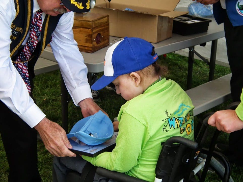 Child in wheelchair receiving a blue cap.