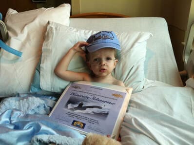 Child in hospital bed holding certificate.