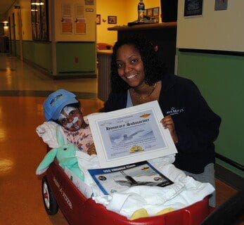 Child in wagon with certificate and woman.